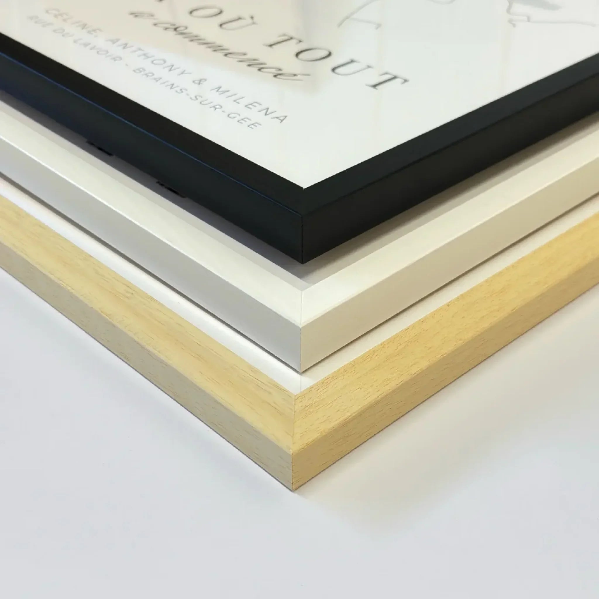 Trois cadres pour affiches en bois naturel, blanc et noir, posés sur une table blanche.