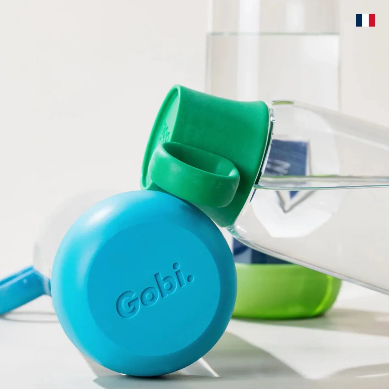 Gourde transparente Gobi avec bouchon bleu et vert, design moderne, drapeau français en fond