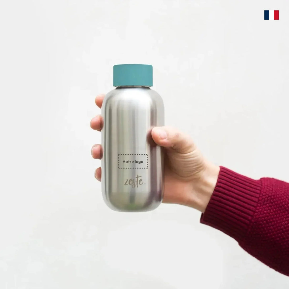 Gourde isotherme inox personnalisable tenue à la main, bouchon bleu, fond neutre.