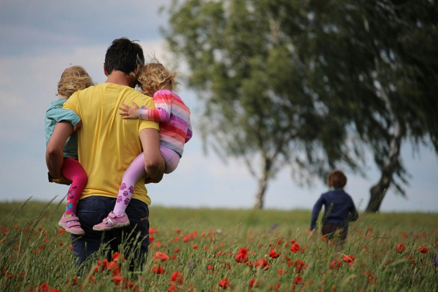 Papa portant deux enfants dans un champ de coquelicots, idées cadeaux fête des pères