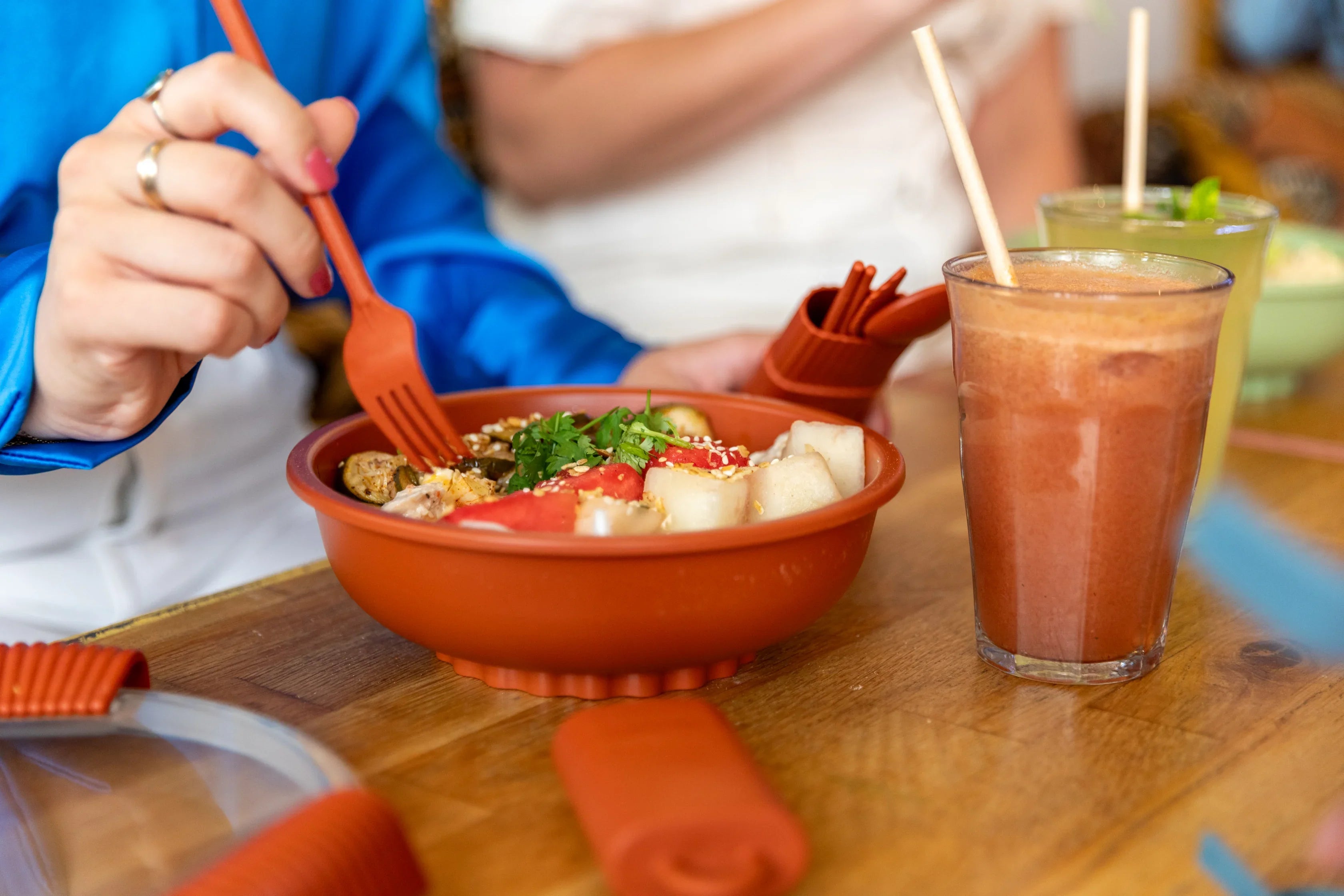 Repas sain dans un bol orange avec fourchette réutilisable et jus, sur table en bois