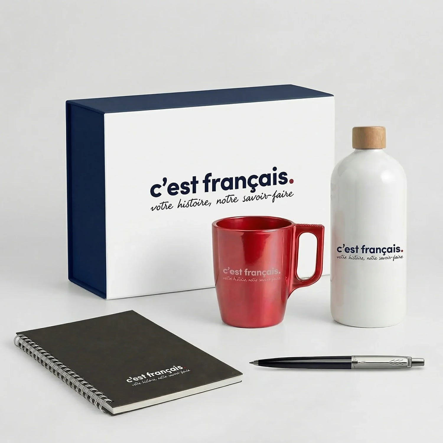 Coffret cadeau personnalisé avec gourde, tasse rouge, carnet et stylo sur fond blanc.