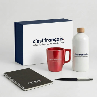 Coffret cadeau personnalisé avec gourde, tasse rouge, carnet et stylo sur fond blanc.